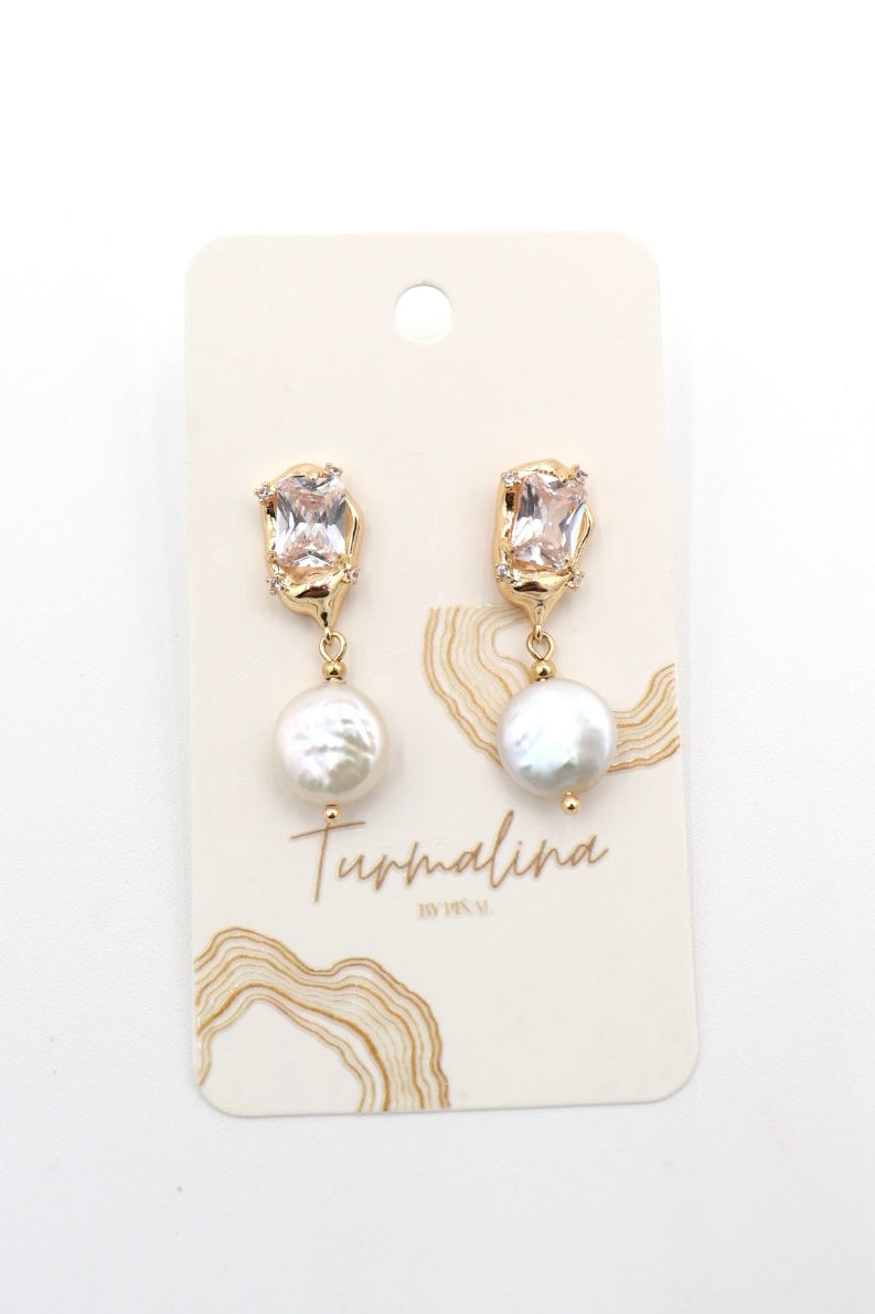 A pair of gold drop earrings with clear faceted stones at the top and white baroque pearls below, displayed on a cream-colored card labeled 'Turmalina by VEVY'.
